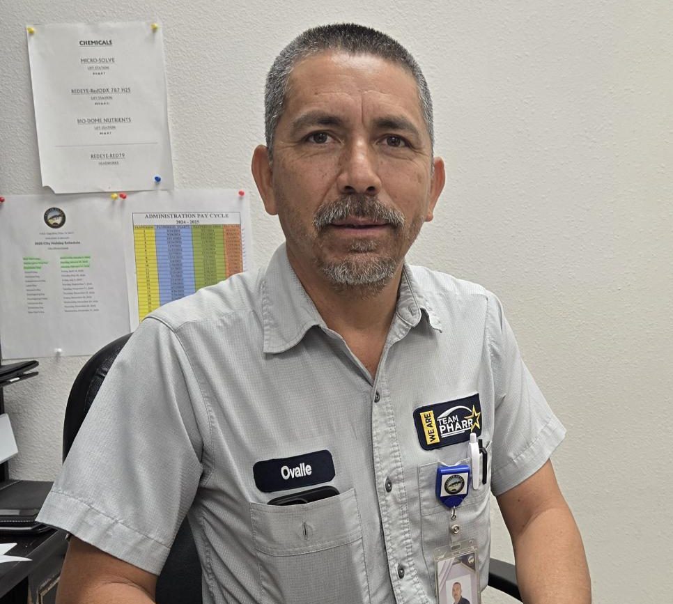 older hispanic man wearing light gray collared shirt seated at his office in front of white wall with papers takced on with colorful thumbtacks